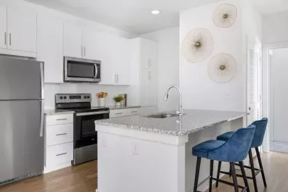 A luxurious kitchen with white cabinetry, granite countertops, stainless steel appliances, and a breakfast bar with plush blue barstools.