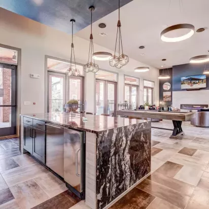 Elegant clubhouse kitchen with a luxurious marble island, modern lighting, and access to the community lounge at The Emerson at Forney Luxury Apartments.