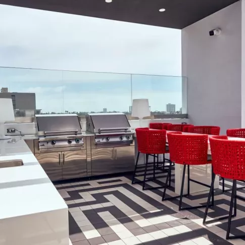 "Rooftop barbecue area at The Linden Luxury Apartments with sleek stainless steel grills, bold red seating, and panoramic city views"