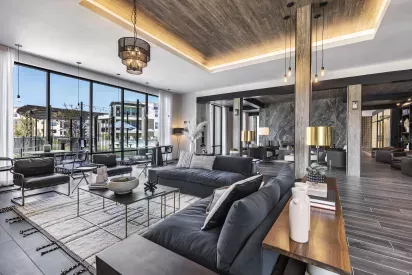 A spacious clubhouse at The Warner Apartments, featuring a striking wood ceiling, a large built-in media wall, and a modern, neutral-toned lounge area with contemporary décor.