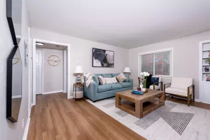 Bright living room with wood-style flooring, a light blue couch, modern artwork, and a large window allowing natural light into the space.