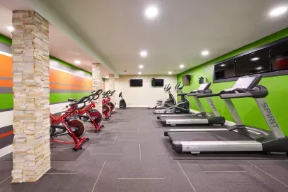 Modern fitness center with treadmills, ellipticals, and bright red stationary bikes lined along a colorful accent wall with stone pillar detailing.