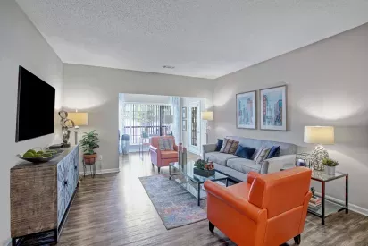 Spacious living room at Amber Chase Apartments with two orange chairs, large sofa, and mounted flat-screen TV.