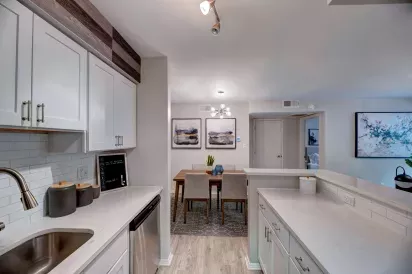 Modern kitchen with white cabinetry, stainless steel appliances, quartz countertops, and a view into a cozy dining area with contemporary decor and warm lighting.