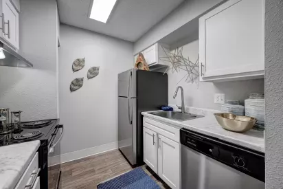 Compact modern kitchen featuring white cabinetry, stainless steel appliances, marble countertops, and decorative wall accents.