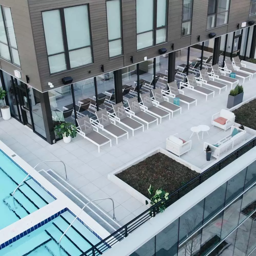 A rooftop pool area at Industry Columbus Apartments featuring a row of modern lounge chairs, cozy outdoor seating, and lush greenery, creating a stylish and relaxing retreat for residents.