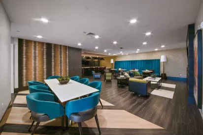 A cozy communal area with plush teal chairs, a large dining table, and warm lighting.