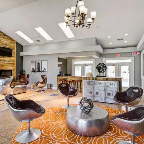 Resident lounge at The Samuel featuring modern aviation-inspired seating, orange patterned rugs, and a rustic wood accent wall with a mounted TV