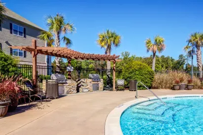 Resort-style outdoor grilling station at Lauren Ridge featuring stone countertops, dual stainless steel grills, and shaded pergolas surrounded by palm trees.