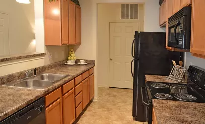 Galley-style kitchen at Market Street Station featuring wood cabinetry, black appliances, and dual sink with granite-look countertops.