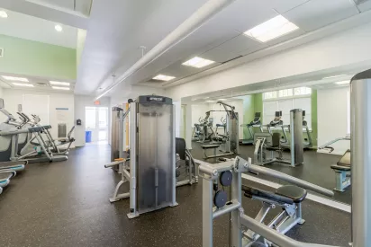 Modern gym interior with various cardio and strength training machines, a dark floor, and a mirrored wall.