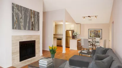 Modern living room with gray sofa, stone fireplace, birch tree painting, and open-plan kitchen and dining area.