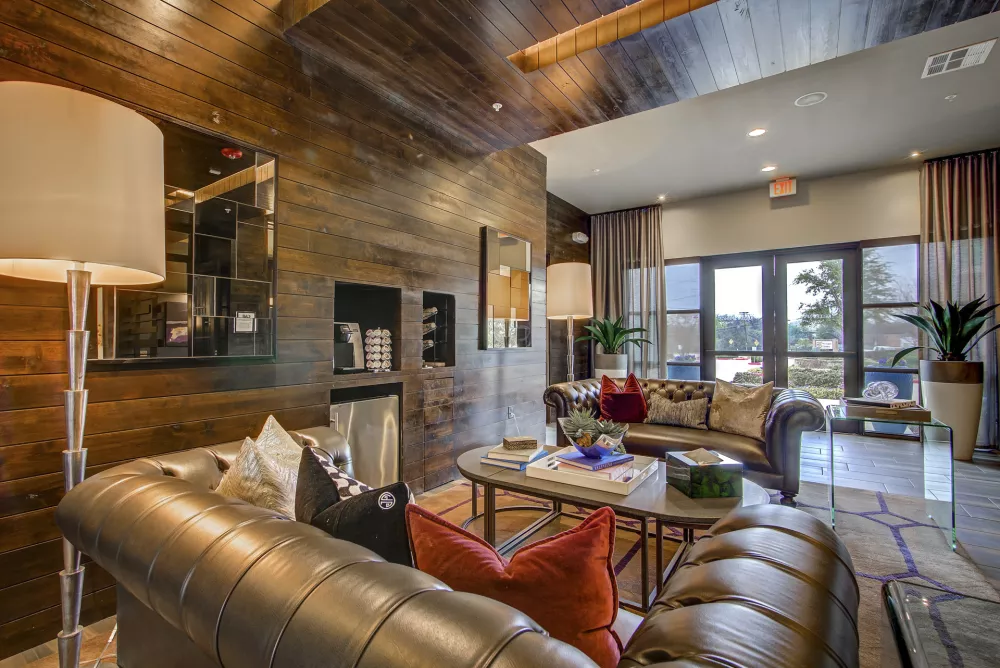 Modern lounge with dark wood walls, comfortable leather sofas, accent pillows, coffee table, and bright patio access.