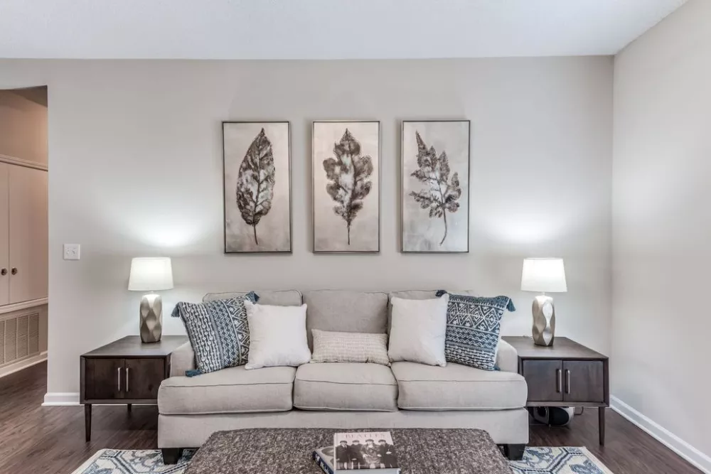 Cozy living room with a beige sofa, three leaf prints, and two lamps on dark side tables.