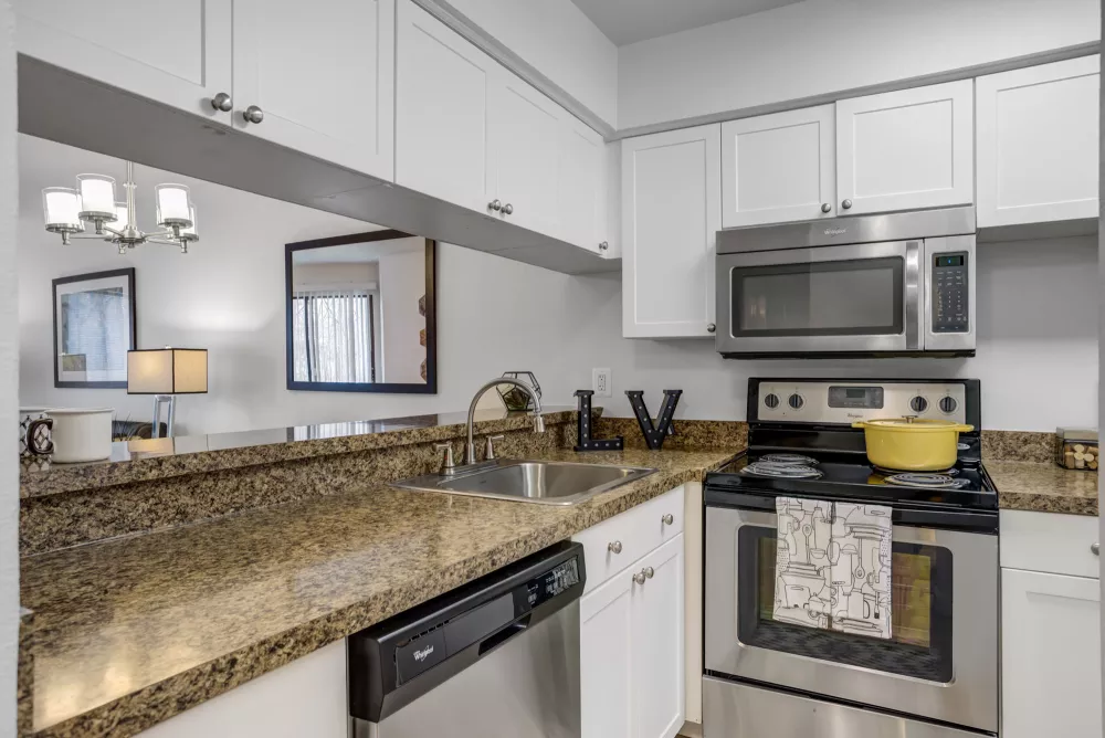 Kitchen with white cabinets, granite counters, stainless steel appliances. Yellow pot on stove, living room in background.