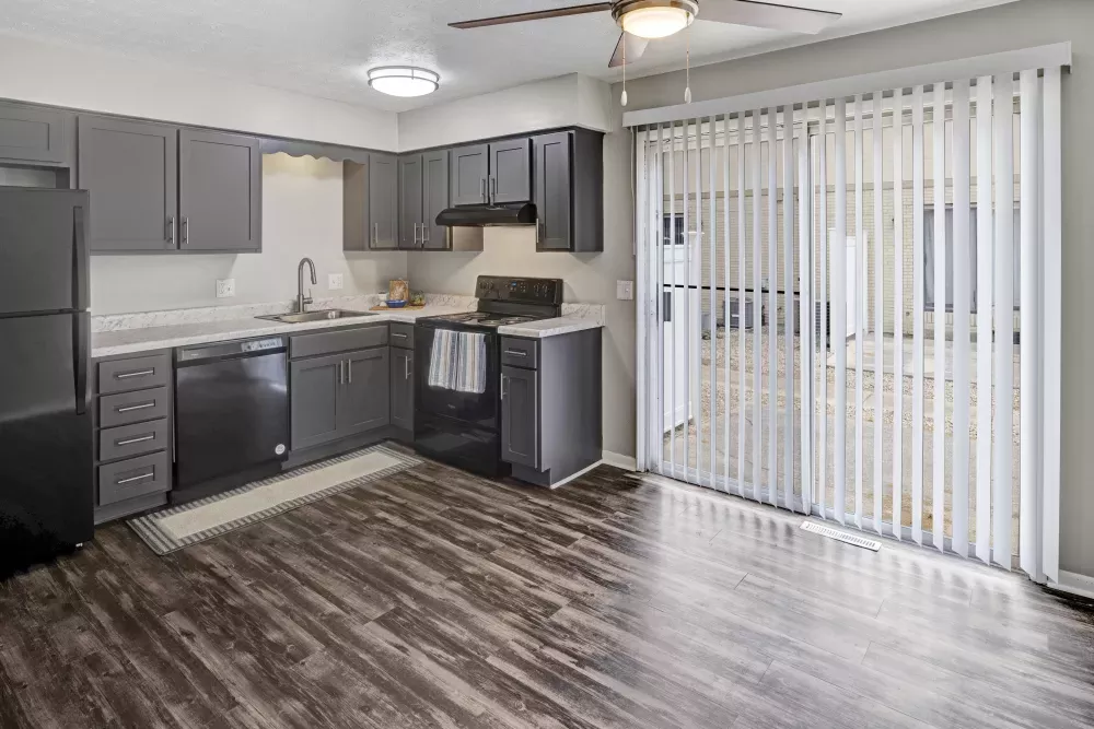 Modern kitchen with dark grey cabinets, dark appliances, wood floor, and a sliding glass door with vertical blinds.