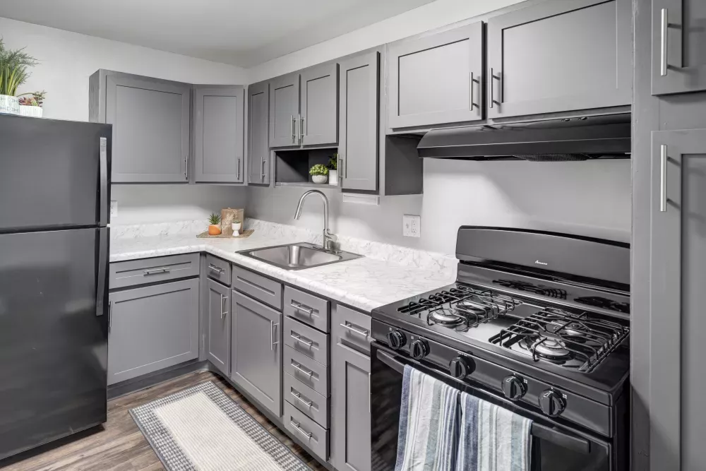 Modern kitchen with gray cabinets, white countertops, black refrigerator and gas stove, and a striped floor mat.