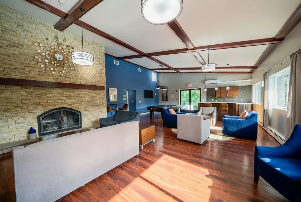 Spacious lounge with a stone fireplace, wood beams, blue accent wall, modern seating, and a pool table.
