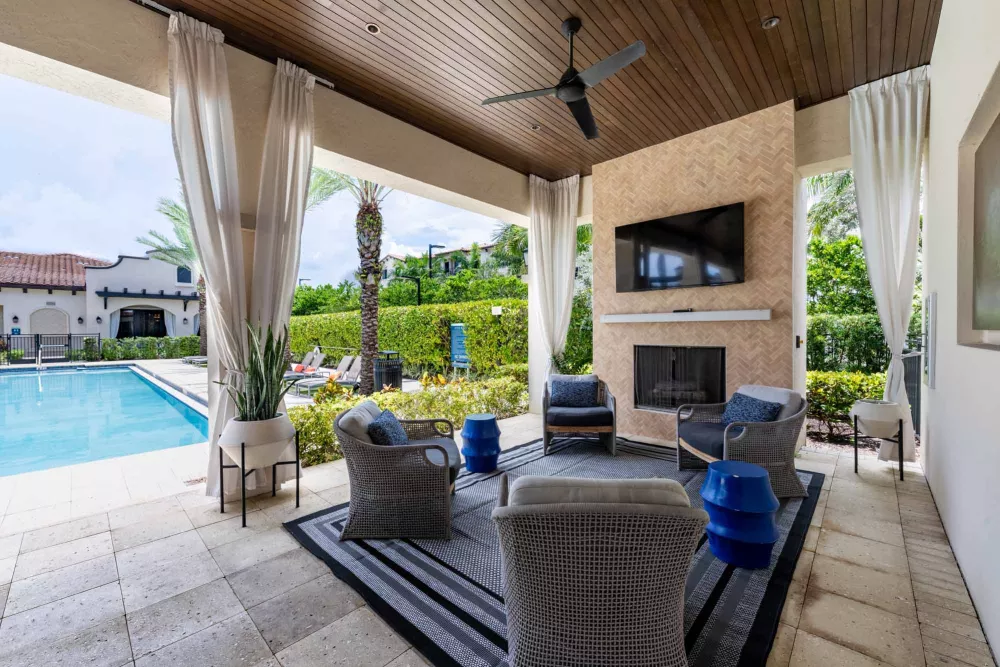 Elegant covered patio with a fireplace, TV, comfortable seating, and a pool view.