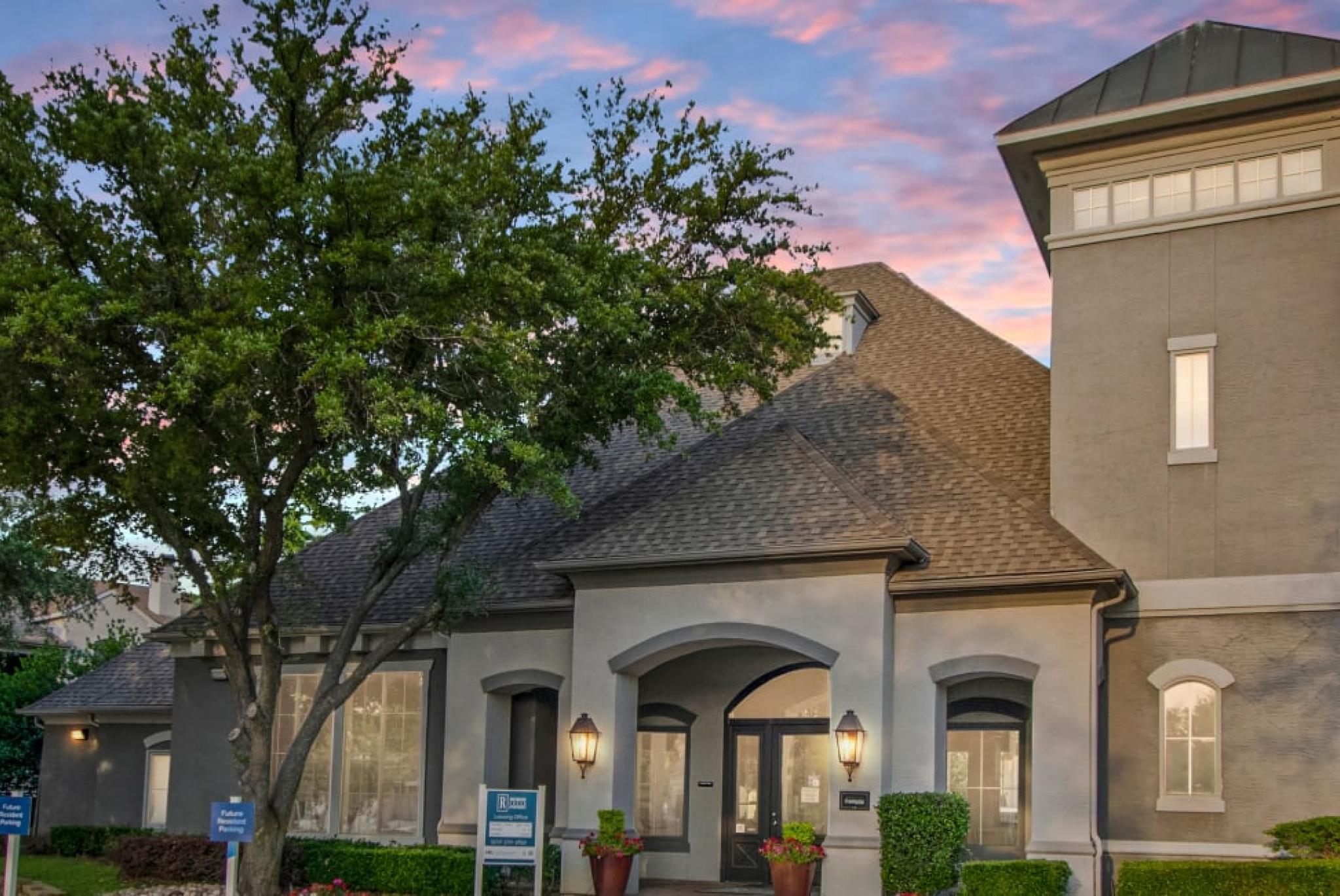 A charming residential building surrounded by lush trees, set against a colorful sunset sky.