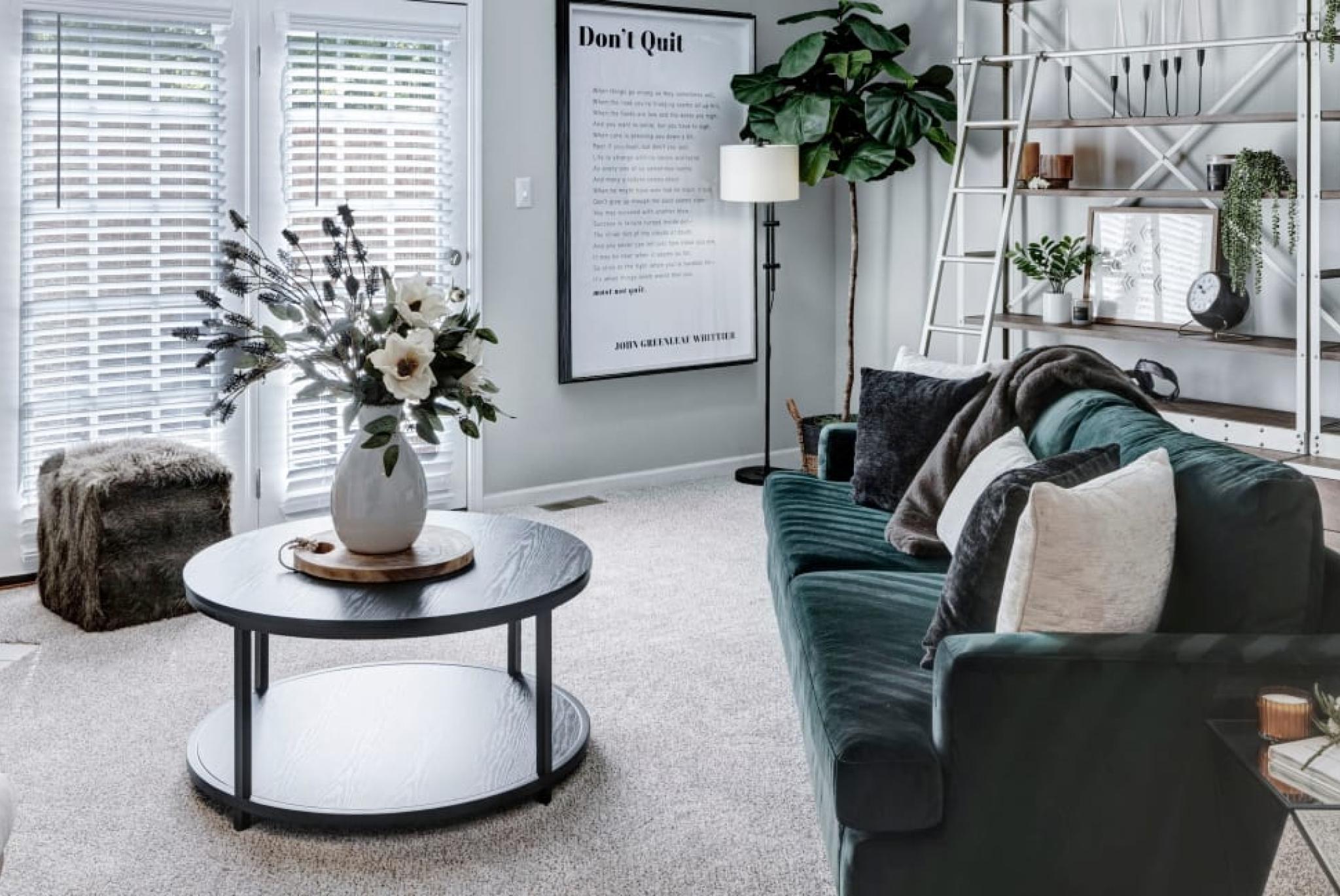 A modern living room with a dark green velvet sofa, cozy fireplace, stylish shelving, and large windows creating a bright and inviting space.