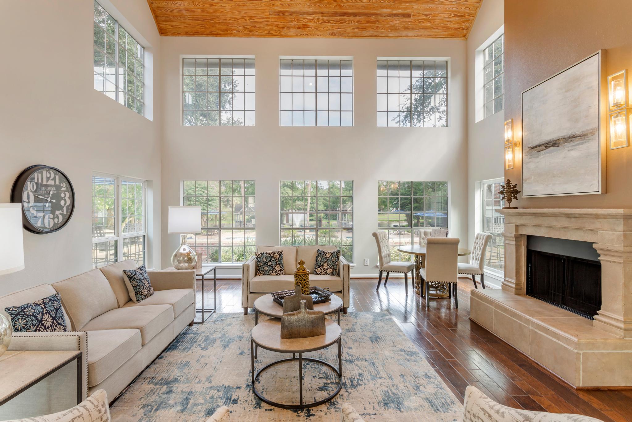 A bright, spacious living room with tall windows, elegant beige sofas, a fireplace, and modern decor accents.