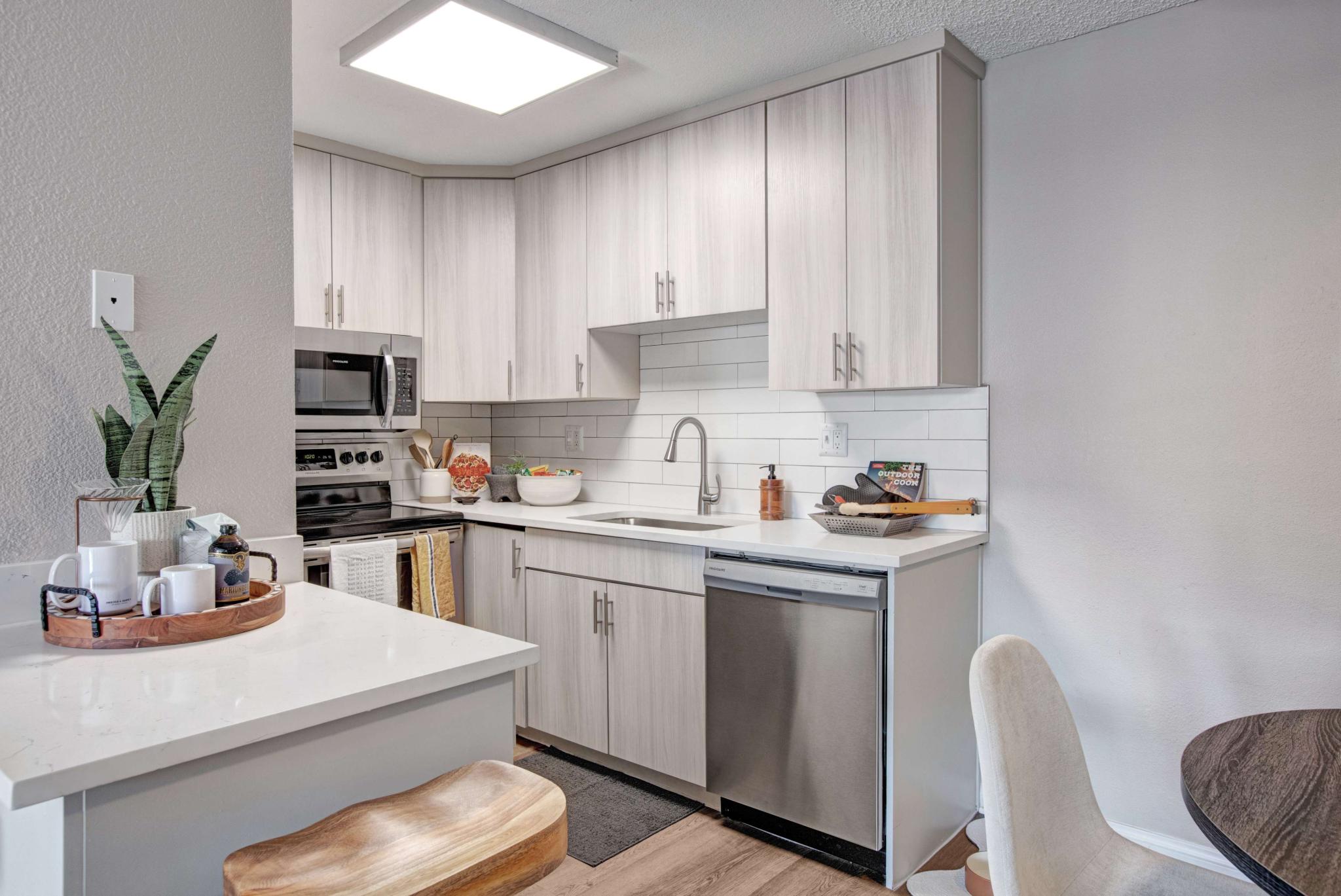 Modern kitchen with stainless steel appliances, white cabinetry, and a small breakfast bar setup.