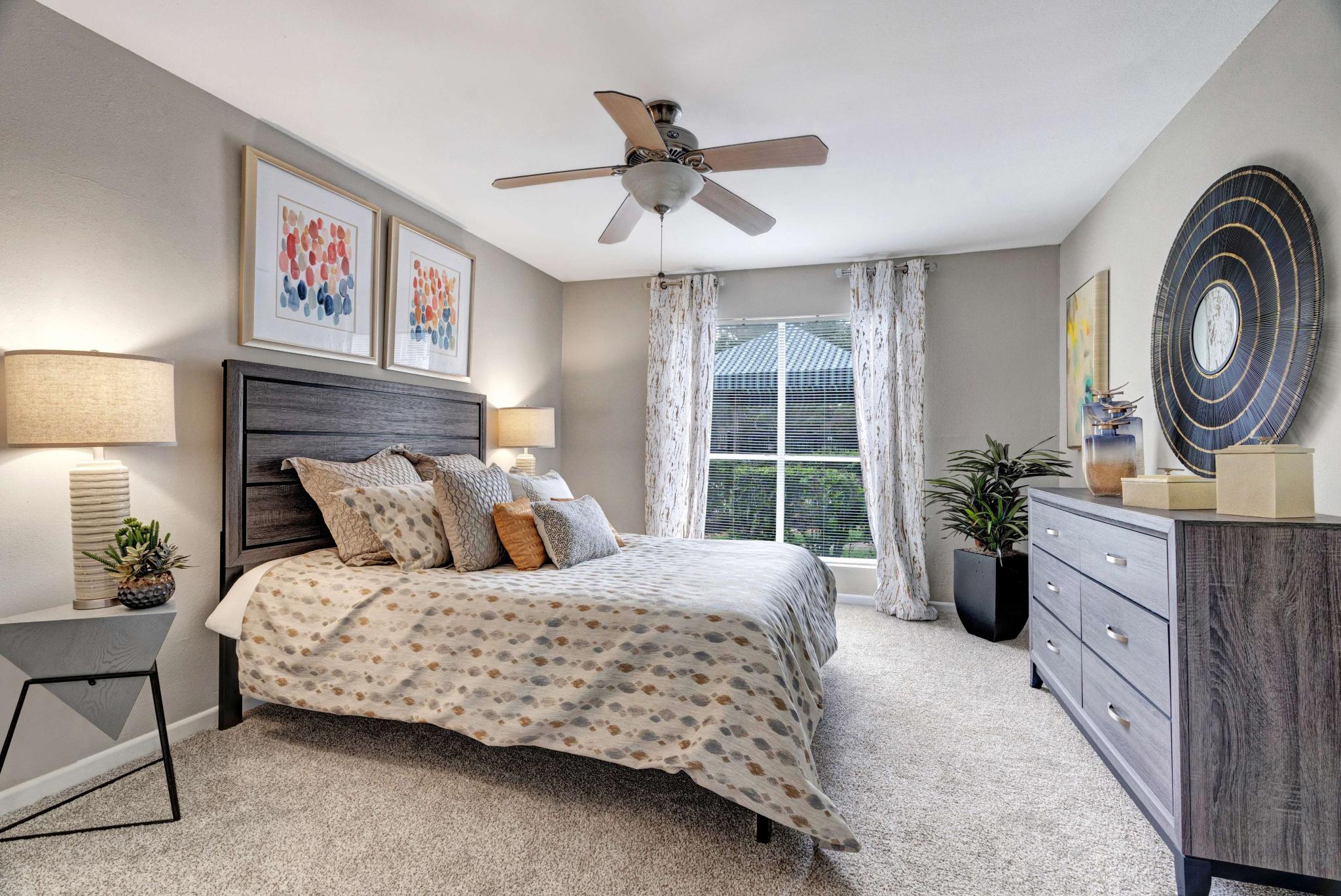 Cozy bedroom with decorative pillows, wall art, and large window bringing in natural light.