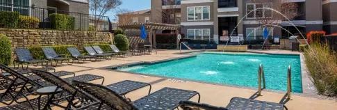 Outdoor swimming pool area with lounge chairs, fountains, and a shaded seating space.