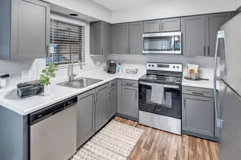 A contemporary kitchen with gray cabinets, marble countertops, stainless steel appliances, and a window above the sink letting in natural light.