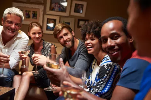 A group of friends enjoys drinks and laughter together in a warmly lit living room.