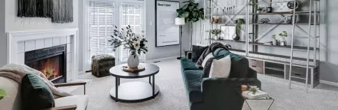 A modern living room with a dark green velvet sofa, cozy fireplace, stylish shelving, and large windows creating a bright and inviting space.