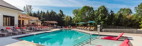 A sparkling outdoor swimming pool surrounded by lounge chairs, umbrellas, and lush greenery, offering a relaxing atmosphere at The Garratt Apartments.
