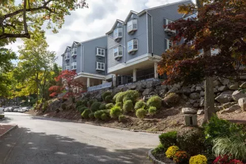 A side view of a residential building with lush greenery and a scenic road.