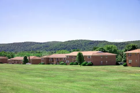 A scenic view of Washington Gardens Apartments in Washington, NJ, surrounded by lush green lawns and picturesque wooded hills in the background. Ideal for highlighting the serene and spacious environment of the community.