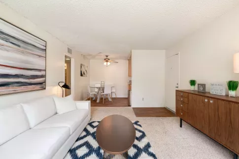 Modern living room with a white couch, abstract artwork, and a round coffee table on a chevron-patterned rug, adjacent to a dining nook.