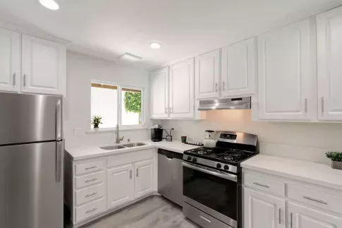 Contemporary kitchen with white cabinetry, stainless steel appliances, and a double sink beneath a window.