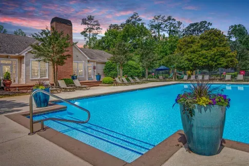 Resort-style swimming pool at Amber Chase Apartments with lounge chairs and landscaped surroundings at sunset.