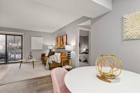 Modern apartment interior with a cozy leather sofa, abstract wall art, and a view of the bedroom and outdoor patio through sliding glass doors, accented by soft lighting and stylish decor.