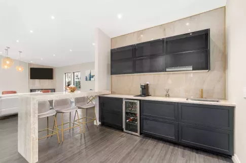 Elegant resident lounge with modern bar seating, a built-in beverage fridge, coffee station, and sleek cabinetry, opening into a spacious common area with soft lighting and contemporary furnishings.