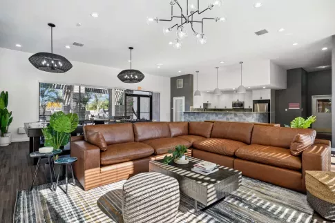 Contemporary clubhouse interior featuring a brown leather sectional, game tables, and open kitchen area with bar seating.