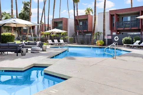 Pool area with lounge chairs, shaded seating, and palm trees at a modern apartment community.