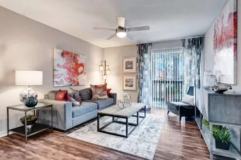Bright and modern living room with a gray sofa, contemporary artwork, and sliding glass doors leading to a balcony.