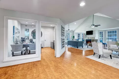 Spacious clubhouse interior with hardwood floors, lounge seating, and large windows allowing natural light to fill the space.