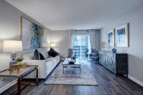 Modern living room with wood-style flooring, contemporary furniture, abstract artwork, and natural light from sliding glass doors.