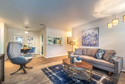 Resort-style swimming pool with stone waterfall feature, surrounded by lounge chairs and blooming trees in a red brick apartment community.