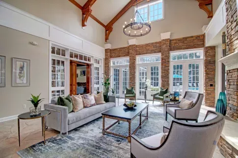 Elegant clubhouse lounge featuring high vaulted ceilings, a chandelier, neutral-toned furniture, and large windows with natural light.