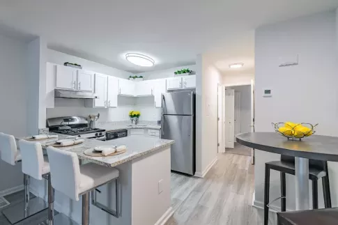 Modern kitchen at Nob Hill Apartments featuring white cabinetry, stainless steel appliances, granite countertops, and a breakfast bar with seating. The space is well-lit with recessed lighting and has a contemporary dining area with a dark table and barstools.
