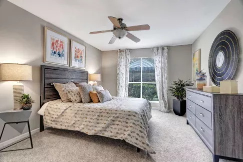 Cozy bedroom with decorative pillows, wall art, and large window bringing in natural light. 