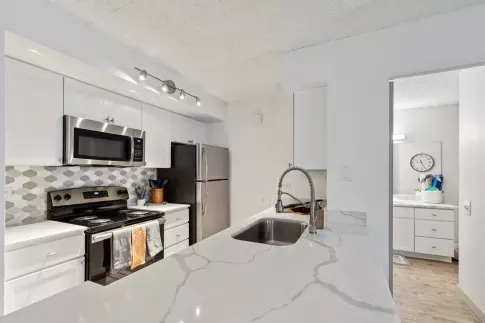 Modern kitchen with white cabinetry, stainless steel appliances, a hexagon tile backsplash, and sleek marble-look countertops featuring a deep undermount sink with a flexible coil faucet.